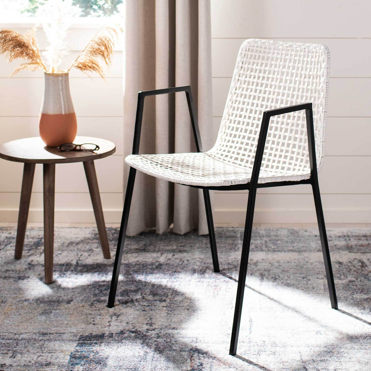 A white woven leather dining chair pairs an airy curved back with sleek black iron arms and legs