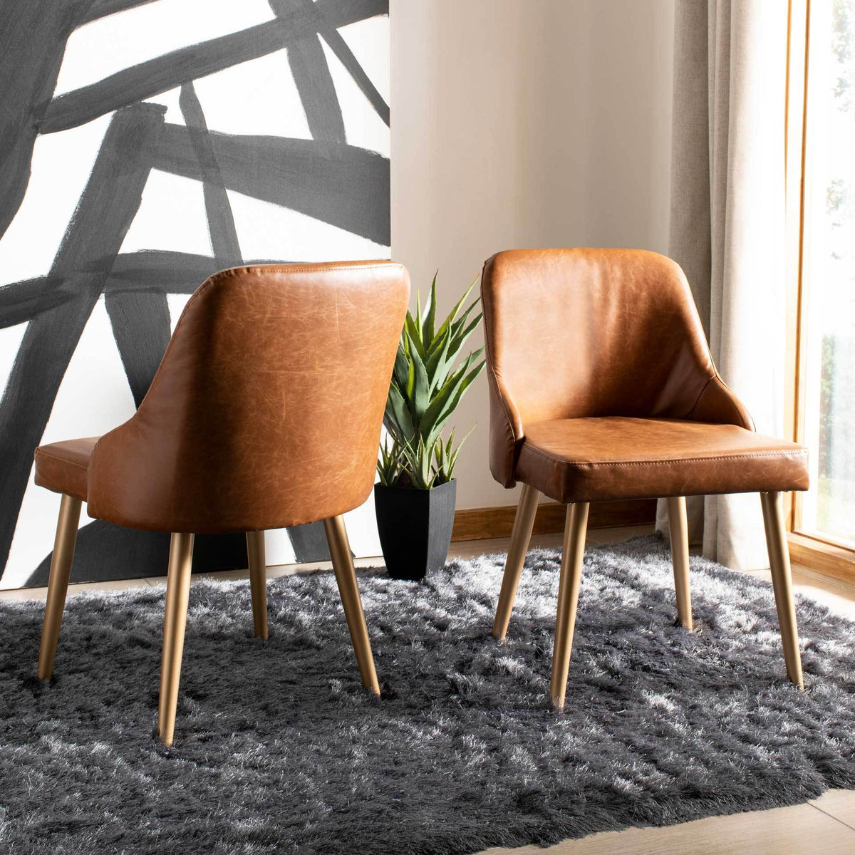 Two warm brown faux leather chairs bring rich texture and slim gold-tone legs to a modern interior.