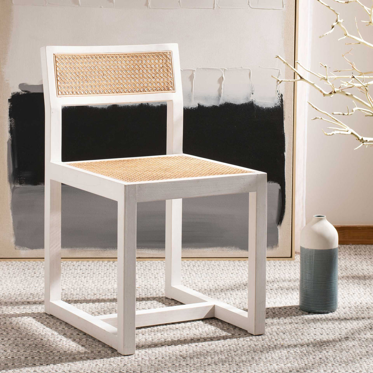 Woven cane adds warmth to a white-painted elm chair set beside abstract wall art