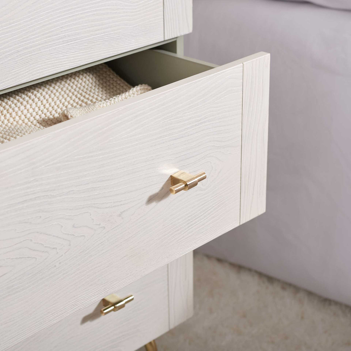 An open whitewashed drawer holds cozy knitwear, with gray sides and gold hardware visible.