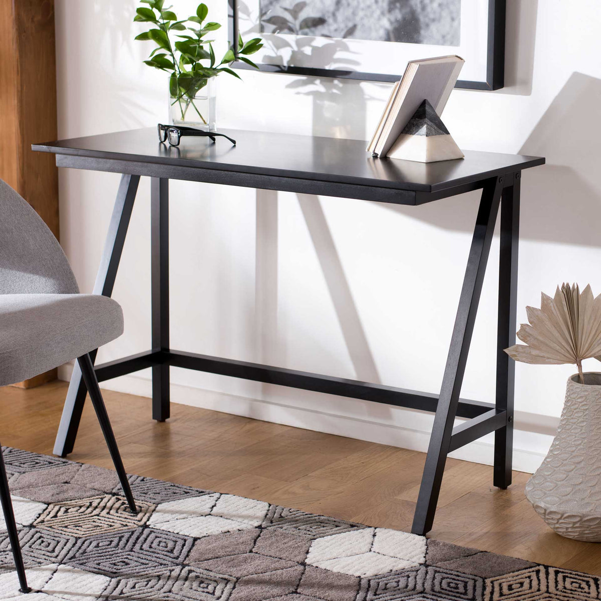 A slim black desk offers a spacious work surface above an open, angled wood frame.