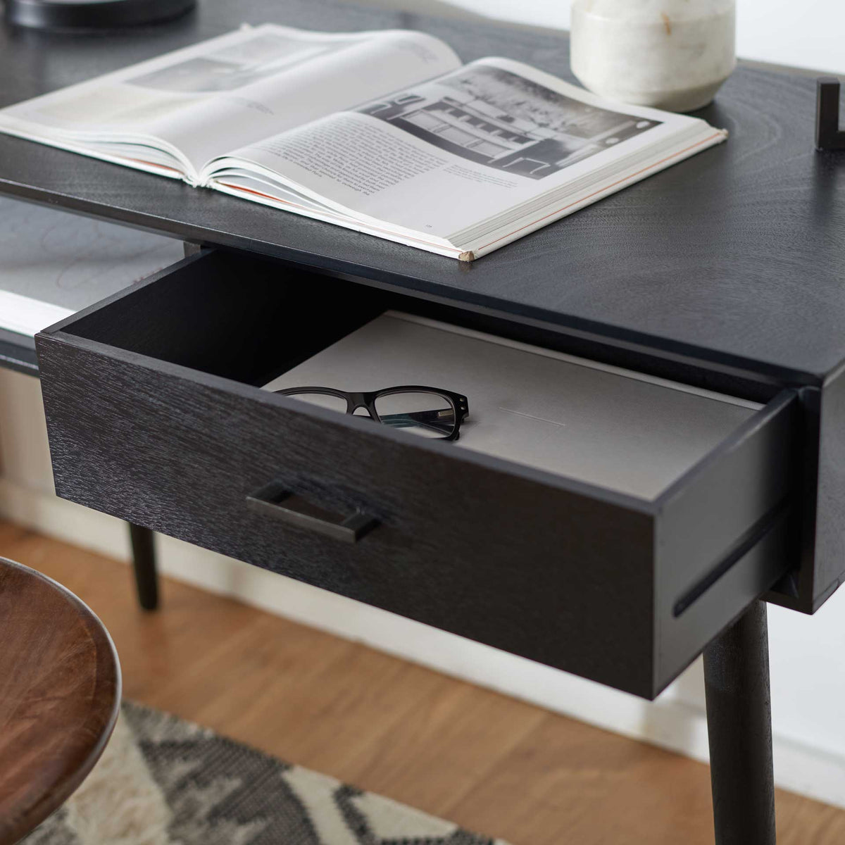 Open black desk drawer keeps glasses and paperwork close at hand beneath the work surface