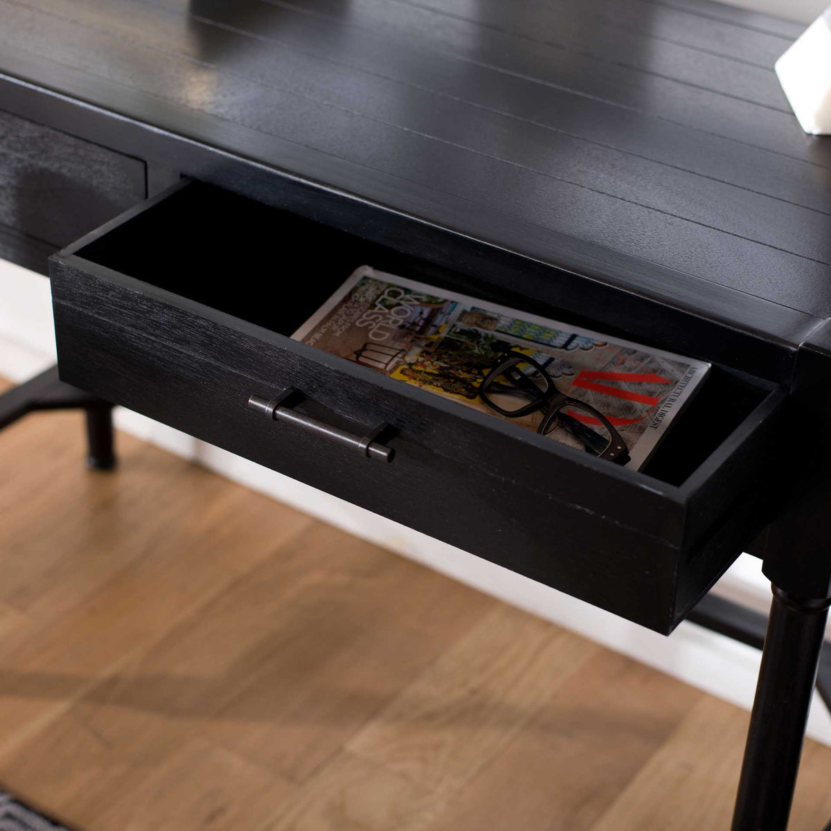 An open black drawer keeps reading materials close at hand beneath the plank-style desktop