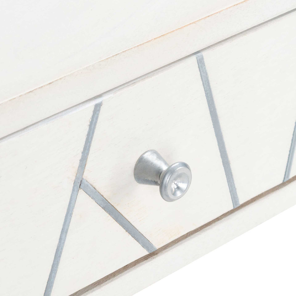A small silver-tone knob punctuates the angular metal inlay across the whitewashed drawer