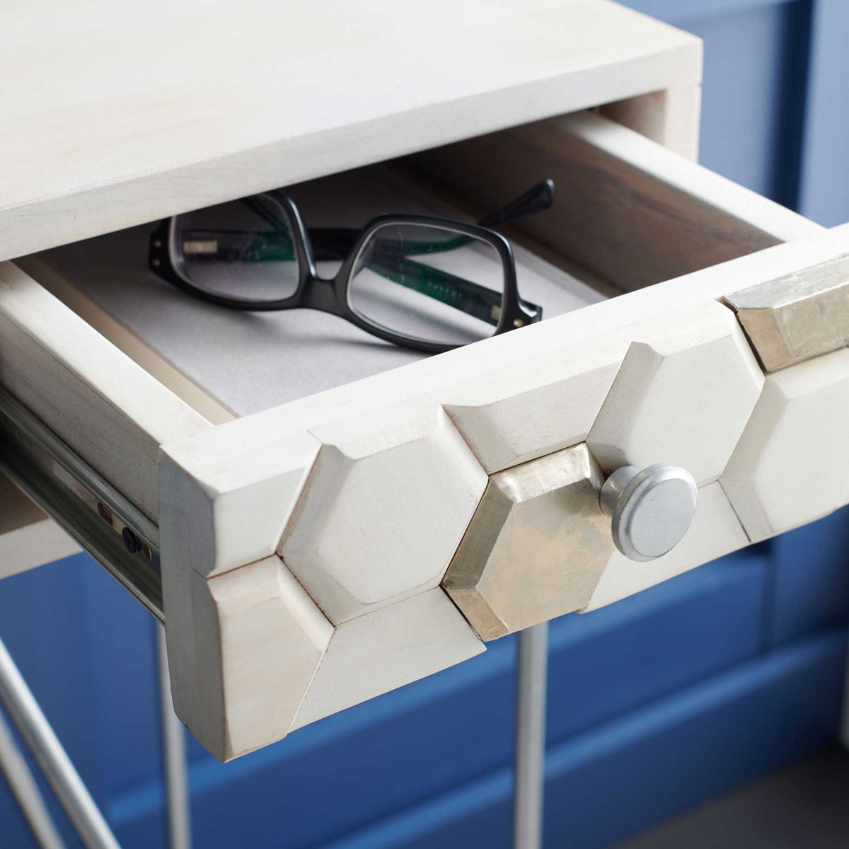 An open honeycomb-front drawer holds eyeglasses beneath the whitewashed desktop, with a round silver pull.