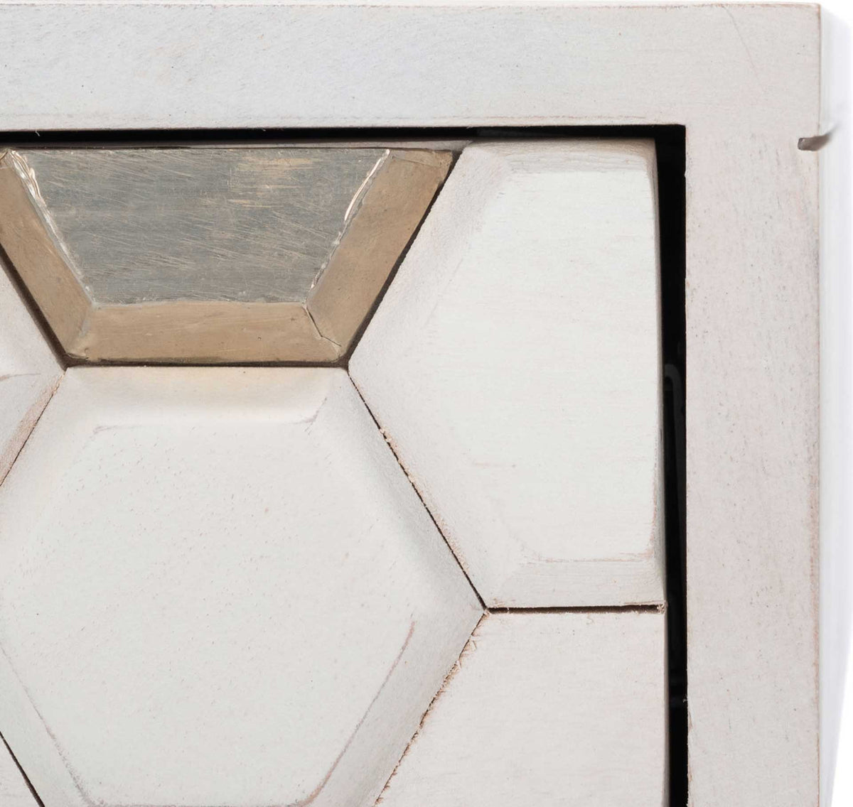 Raised honeycomb carvings and metallic silver inlays texture the whitewashed drawer front.