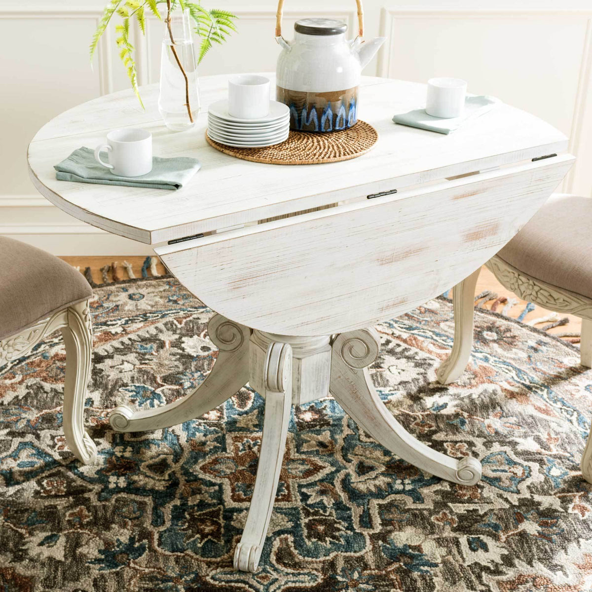 One hinged leaf lowers for flexible dining on this antique white table with a carved pedestal base