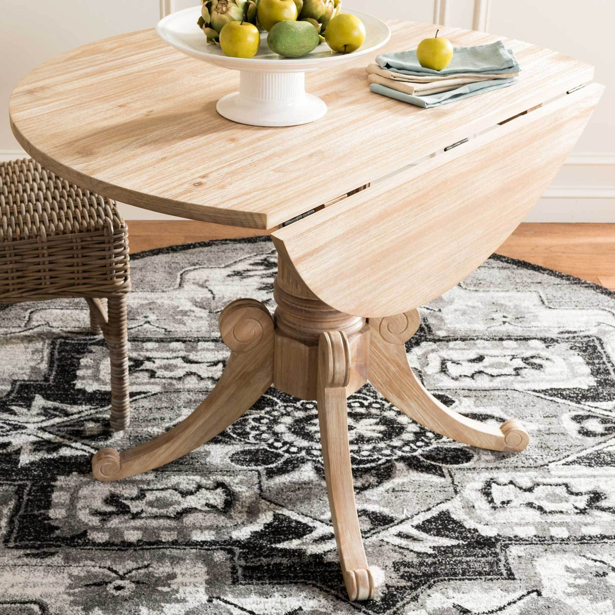 Warm natural wood grain highlights the hinged drop leaf and sculpted pedestal of this versatile table