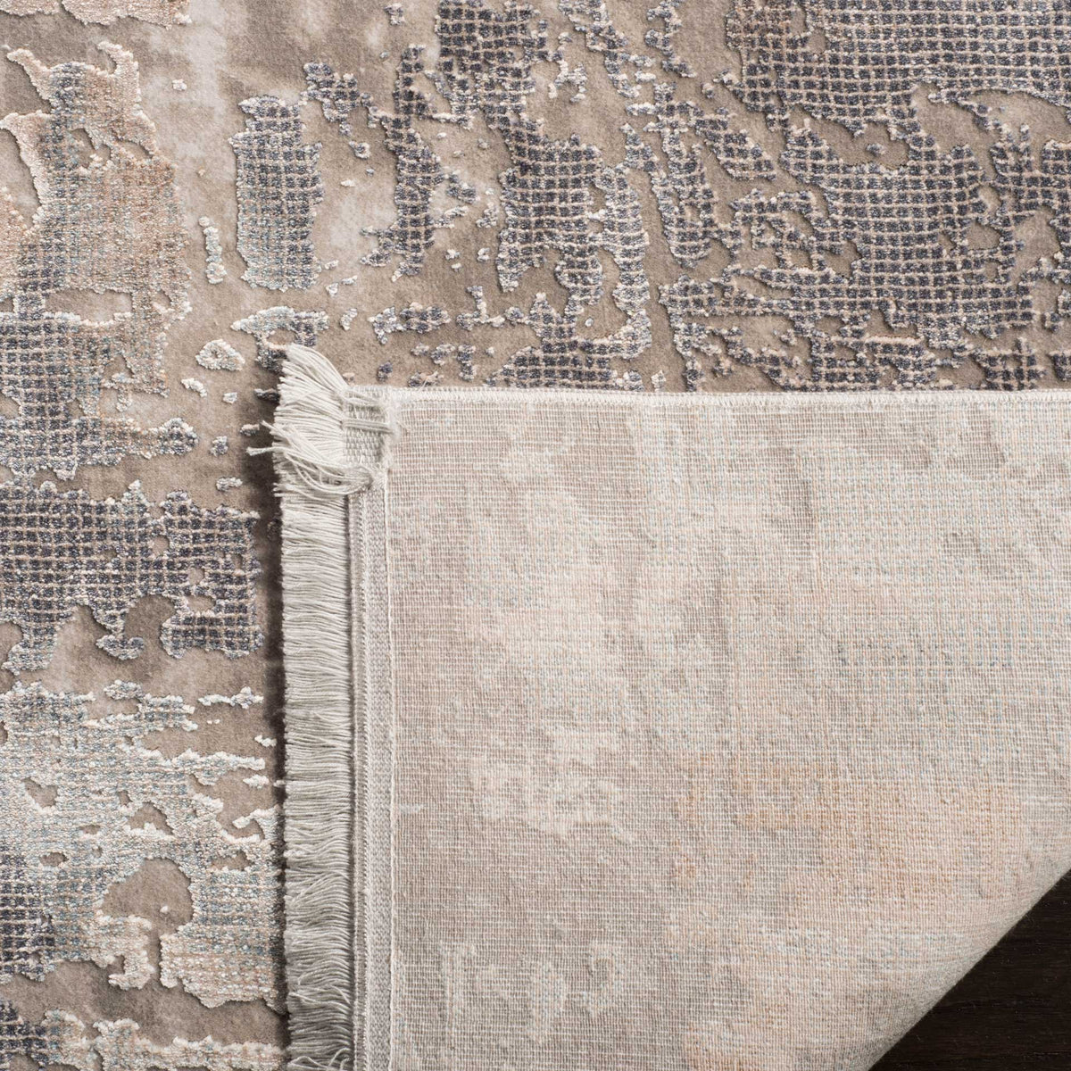A folded corner reveals the rug's woven cotton backing beside its textured abstract surface