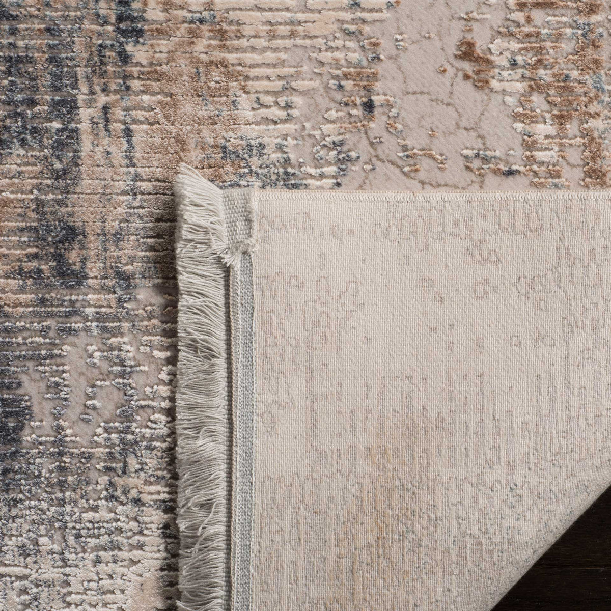 A folded corner reveals woven cotton backing beneath the abstract pile and fringed edge.