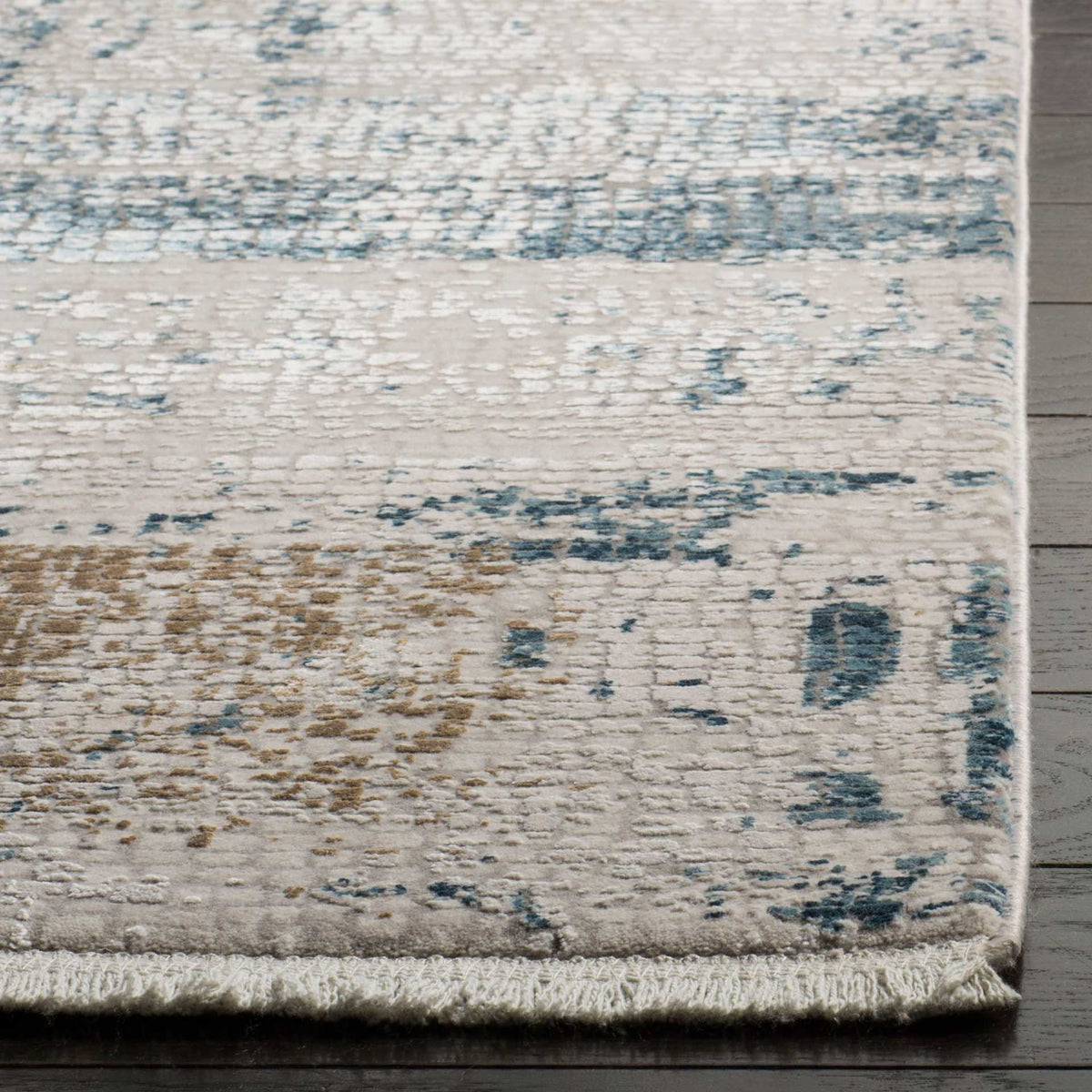 Short fringe trims the rug's textured edge beside faded blue and warm taupe markings.