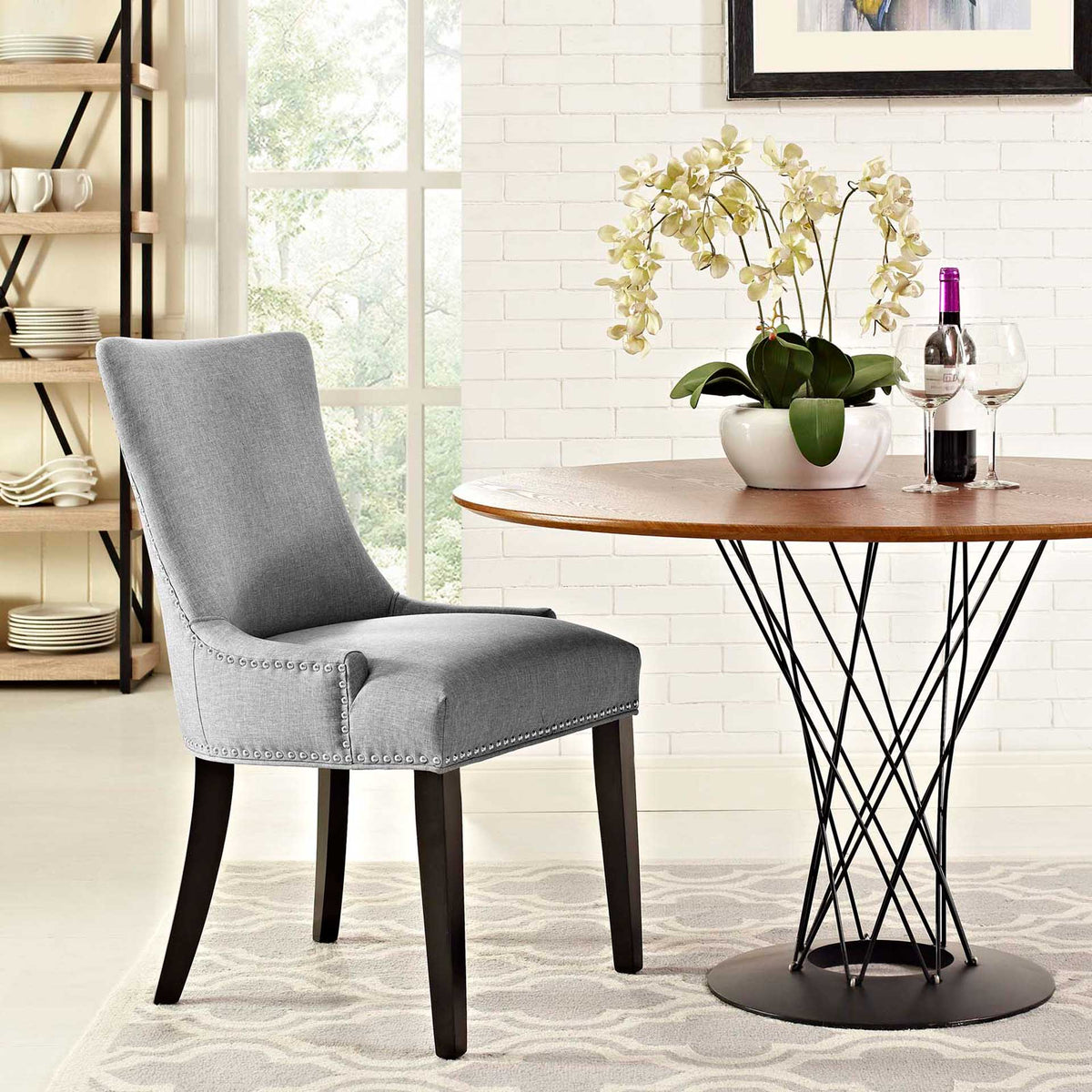 A cushioned light gray chair with a curved back and silver nailhead trim adds comfort to a bright dining nook
