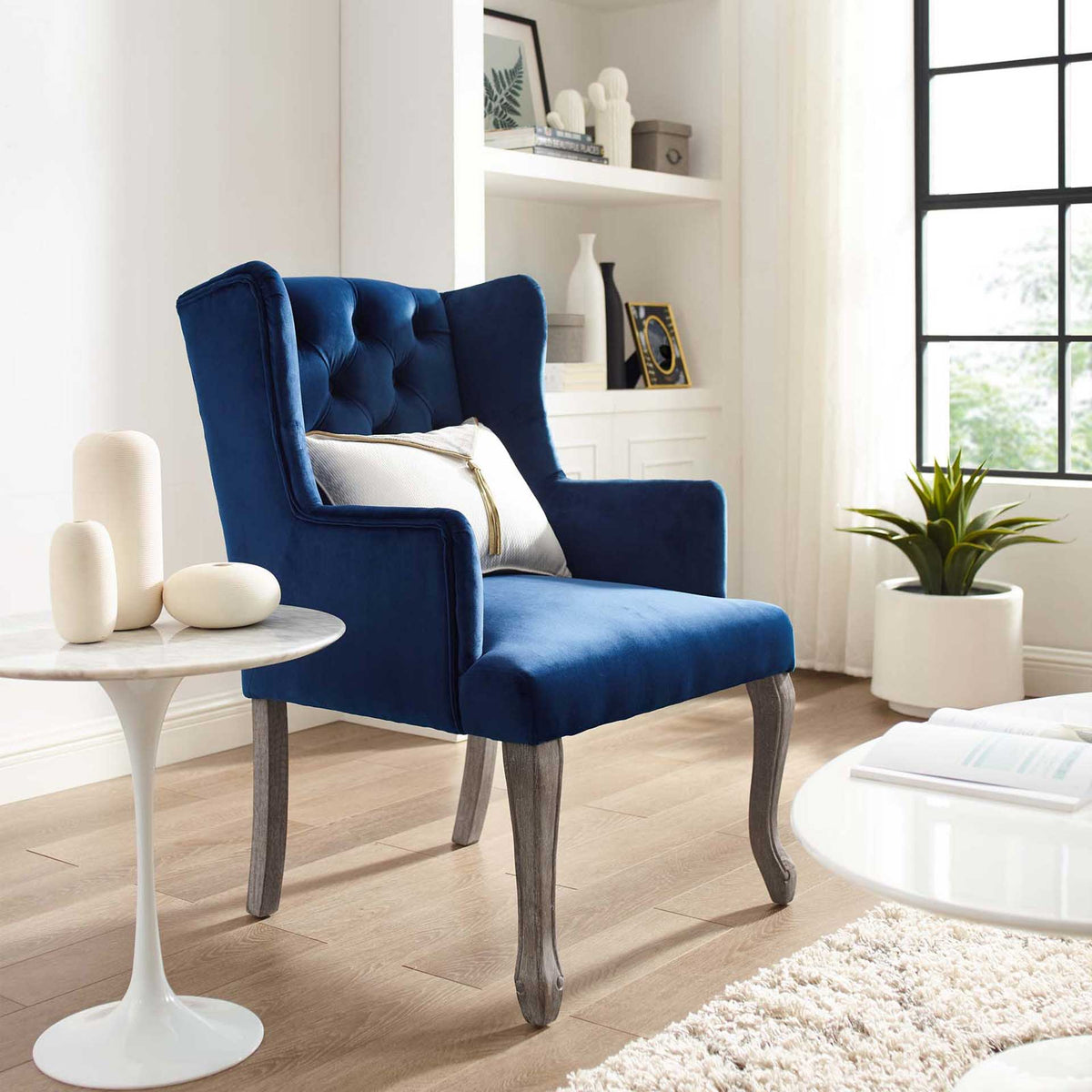 A navy velvet tufted wingback and weathered wood legs bring warmth to a bright living area