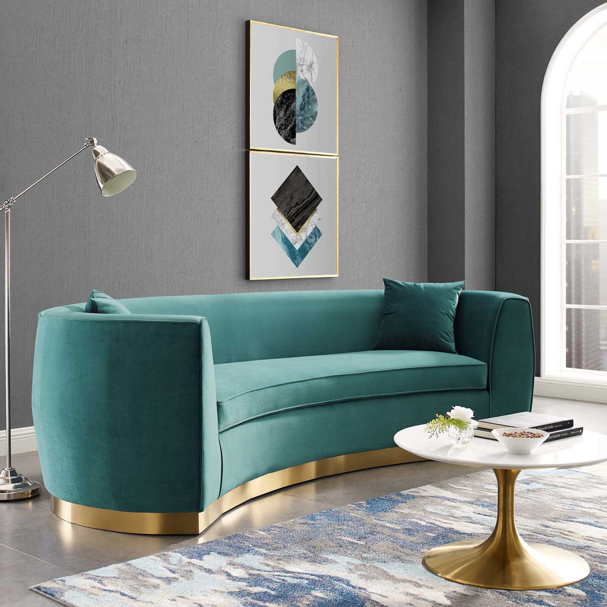 A curved teal velvet sofa brings plush seating and warm gold accents to a modern living room
