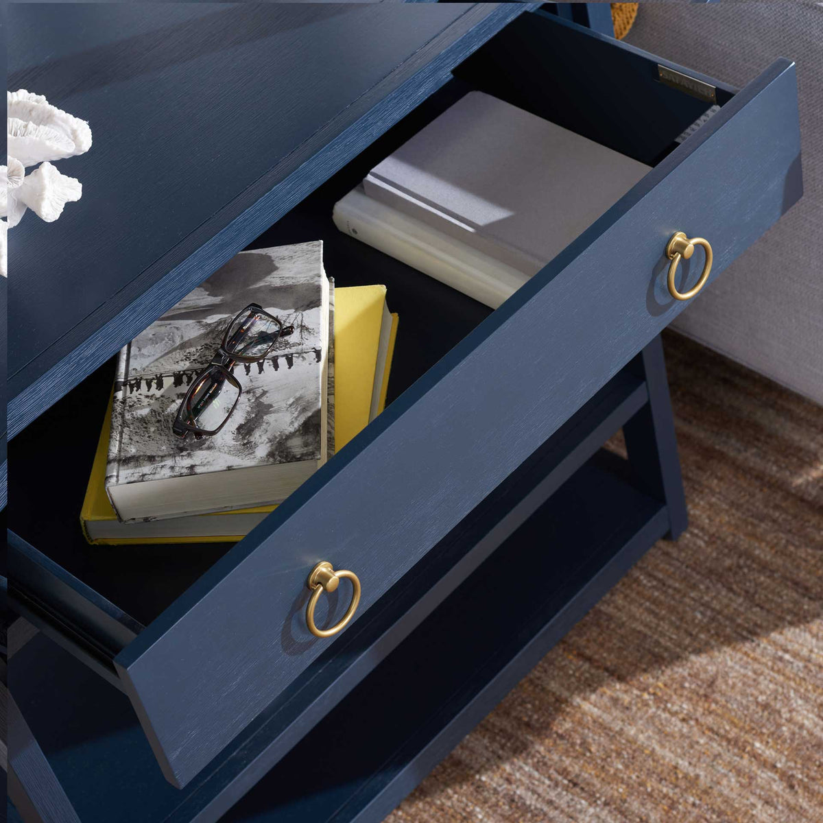 An open navy drawer holds books and accessories, with gold ring pulls on its face.