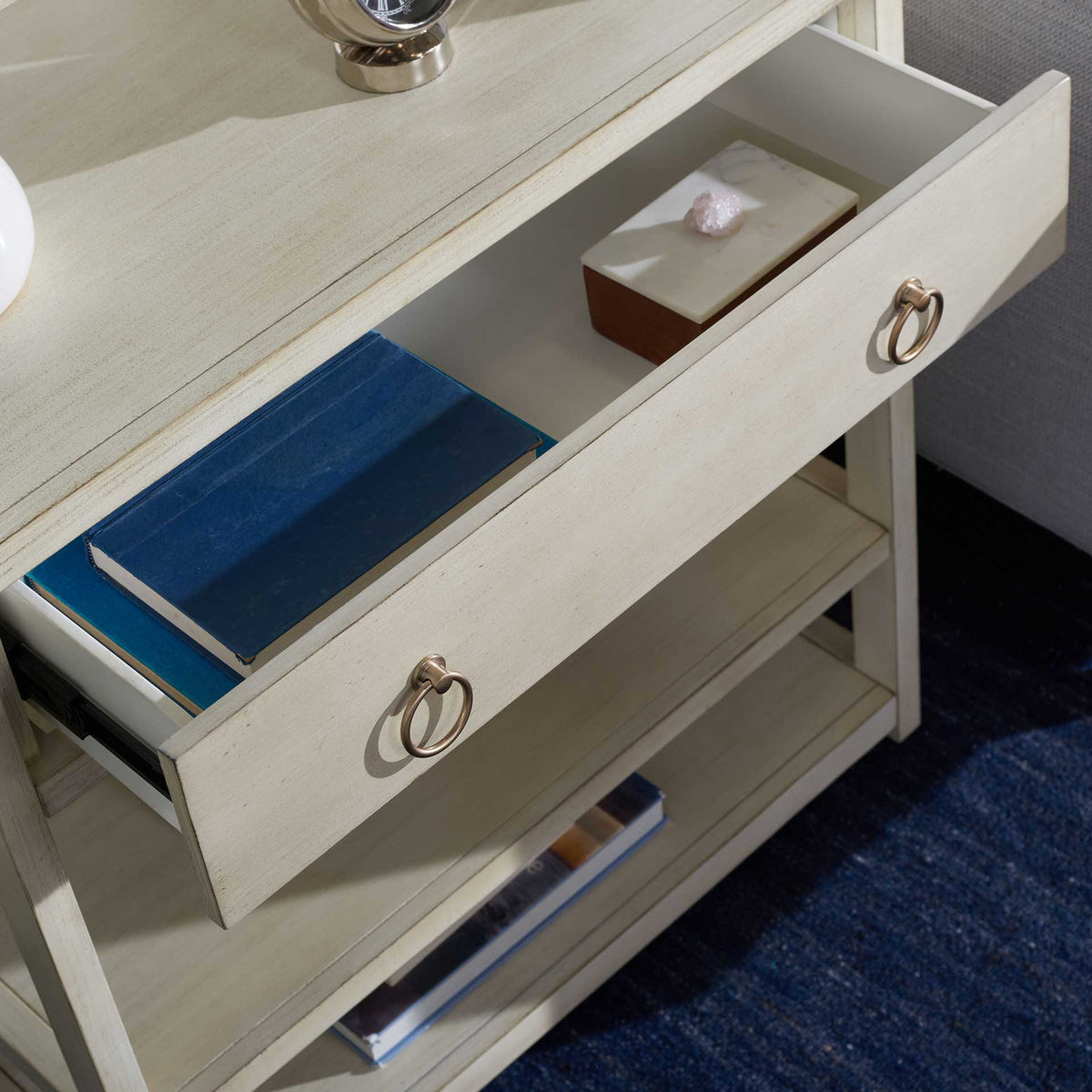 Gold ring pulls accent an open antique white drawer holding books and small accessories.