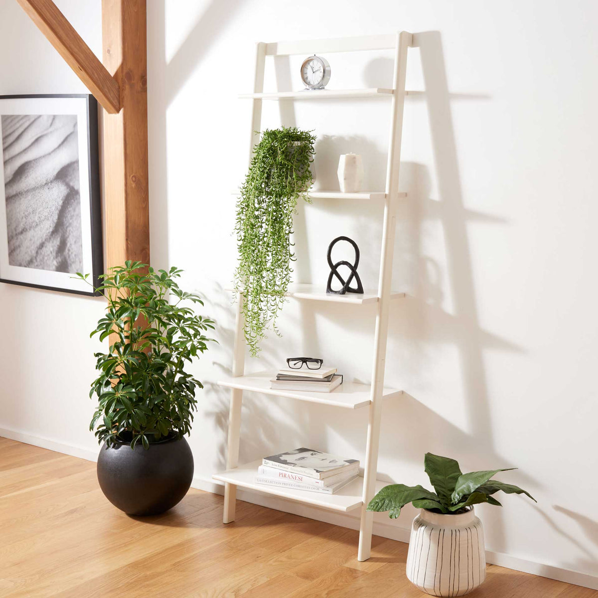 White leaning shelves hold books, plants and sculptural decor in a bright room.