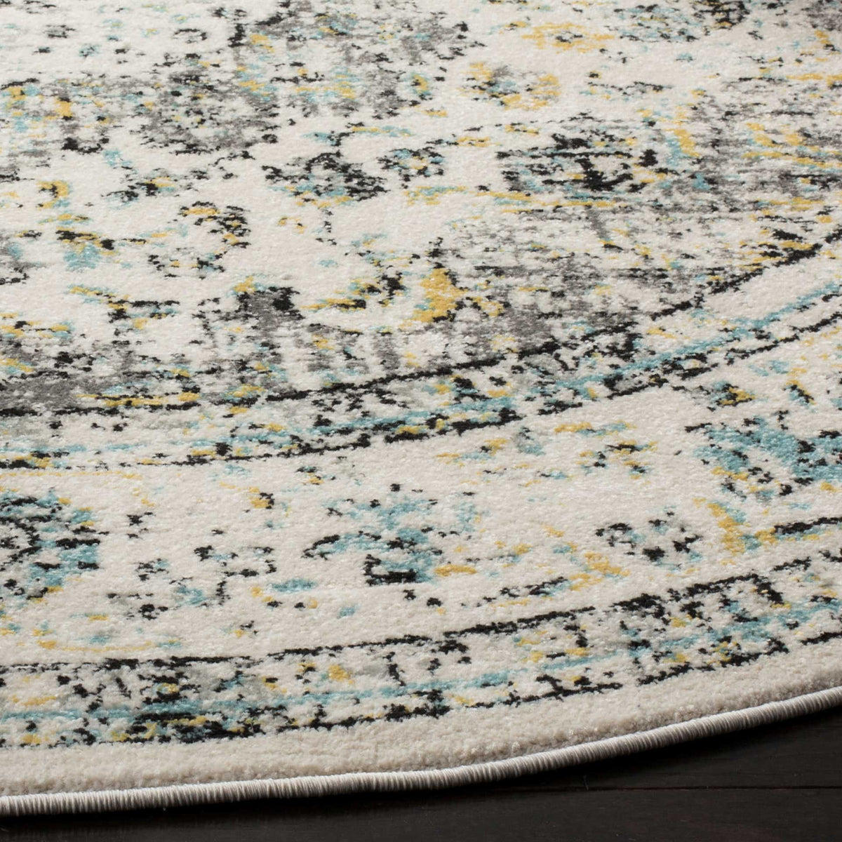 A curved bound edge finishes ivory pile patterned with weathered gray, gold, and teal details.