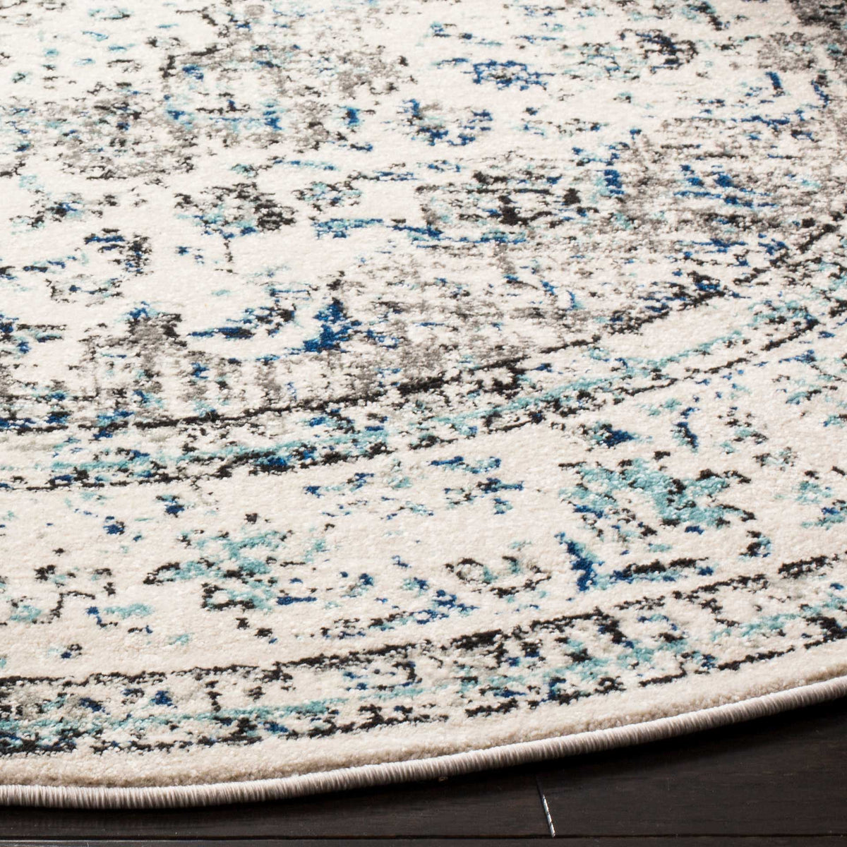 A neatly bound edge frames distressed gray, navy, and teal details across an ivory pile.
