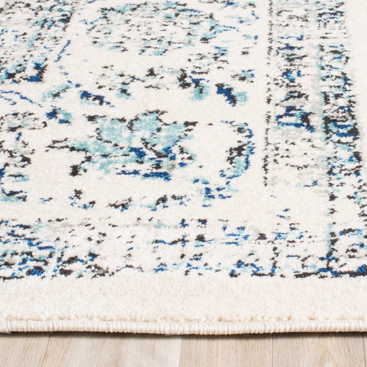 Ivory pile shows blue and gray floral traces beside a neatly finished rug edge