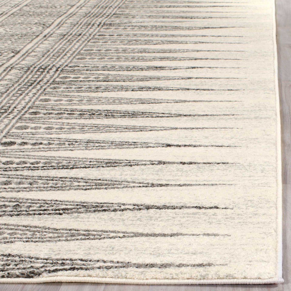 Tapered gray lines cross an ivory pile beside a neatly bound rug edge.