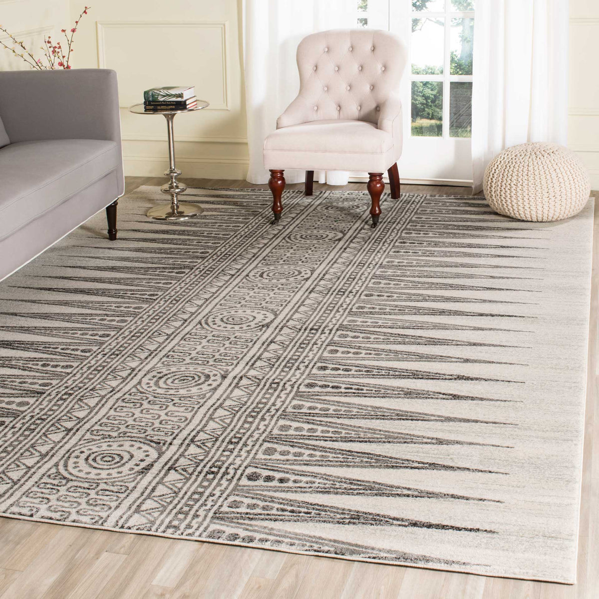 Ivory and gray geometric rug brings patterned warmth beneath a chair and sofa in a bright living room.