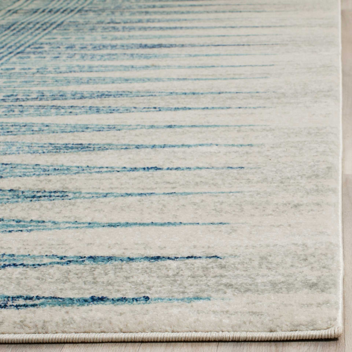 Bound ivory rug edge meets soft pile patterned with narrow turquoise strokes.