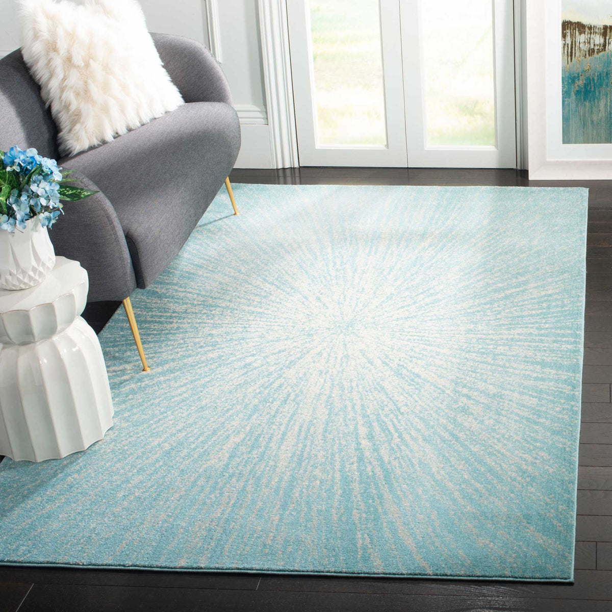 An aqua and ivory starburst rug brightens a seating area with a gray sofa and dark wood floors.
