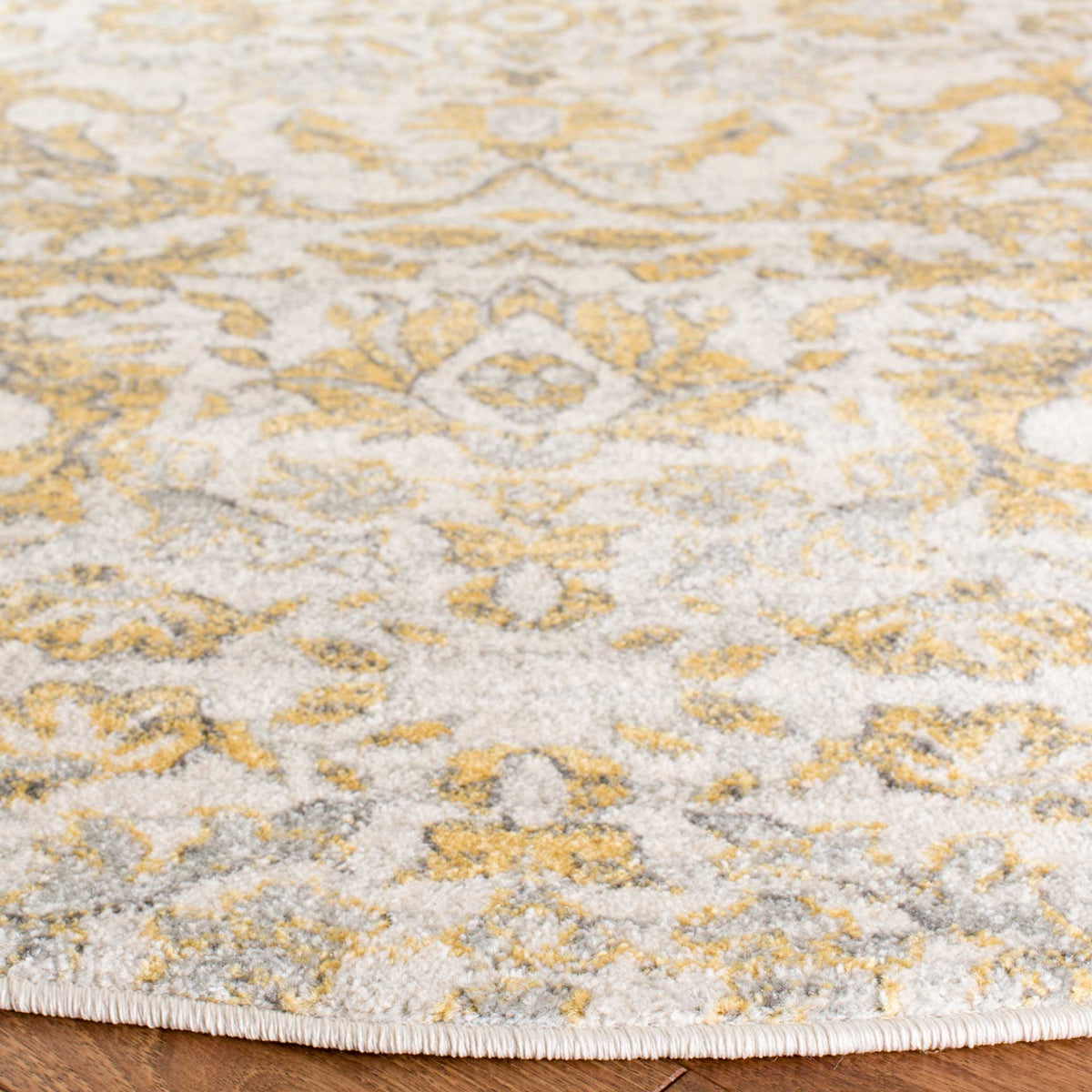 A neatly bound edge accents the soft ivory pile and intricate gold and gray floral pattern