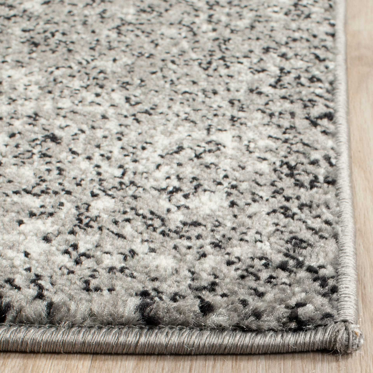Soft gray and ivory yarns form a textured surface along a bound rug corner