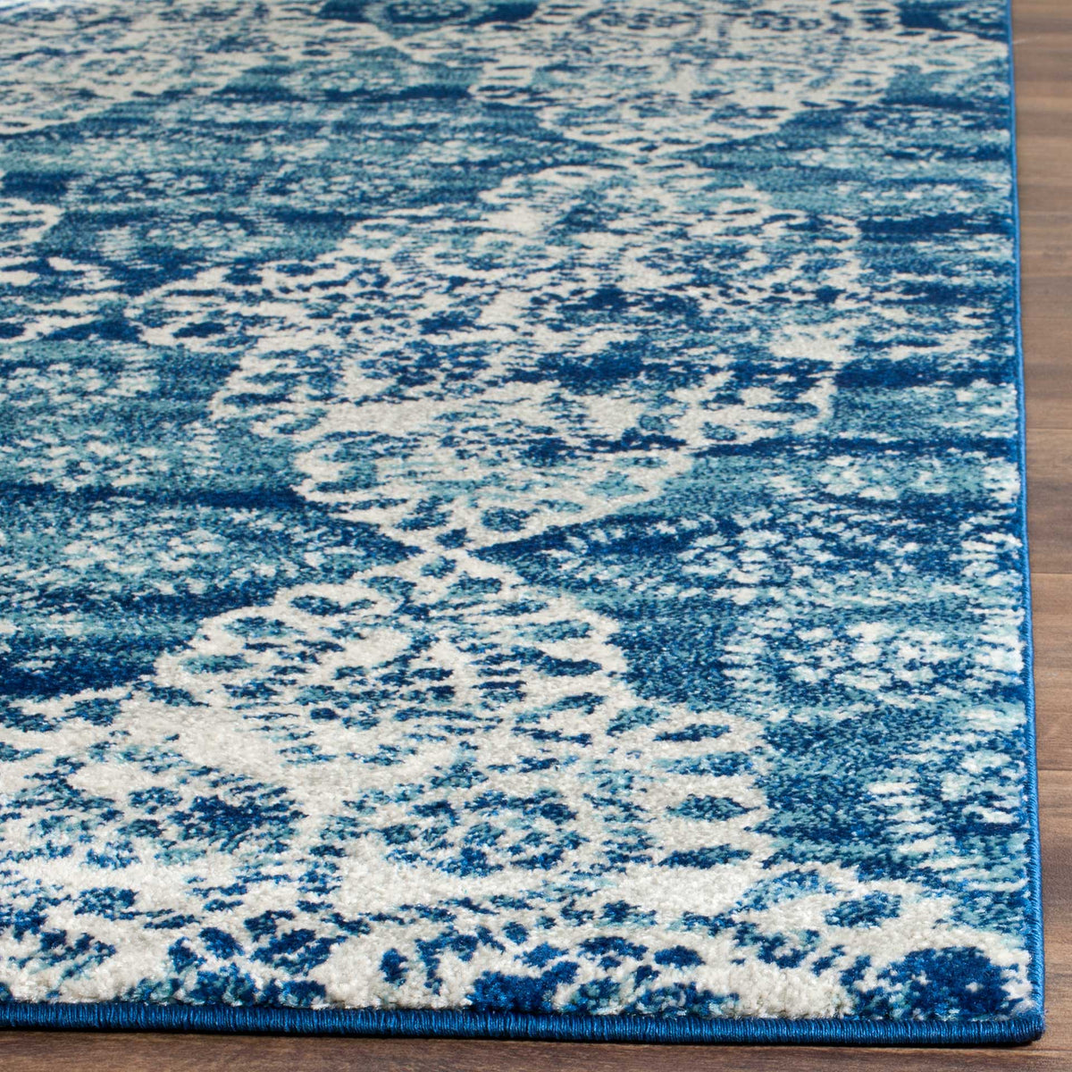 Intricate ivory florals sweep across royal blue pile with neat blue binding at the edges