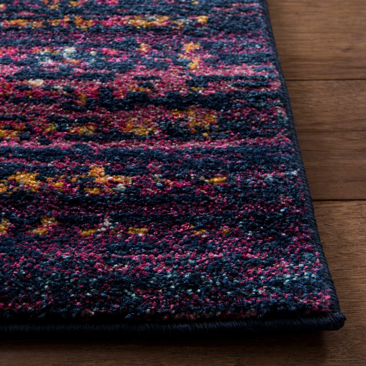 Textured navy and fuchsia pile meets a neat bound edge, dotted with warm amber flecks.