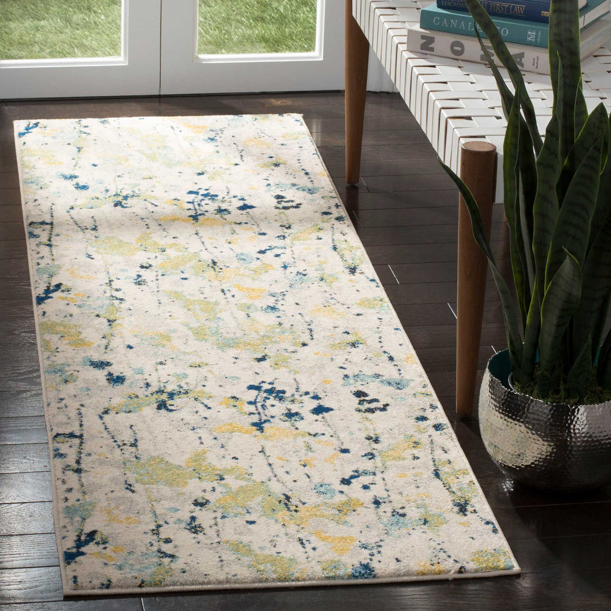 Yellow and blue abstract accents add subtle color to an ivory runner beside a woven bench
