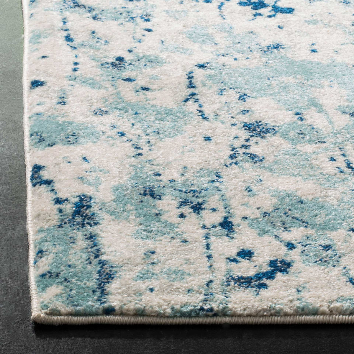Bound edges finish a soft ivory pile with aqua patches and deep blue speckles