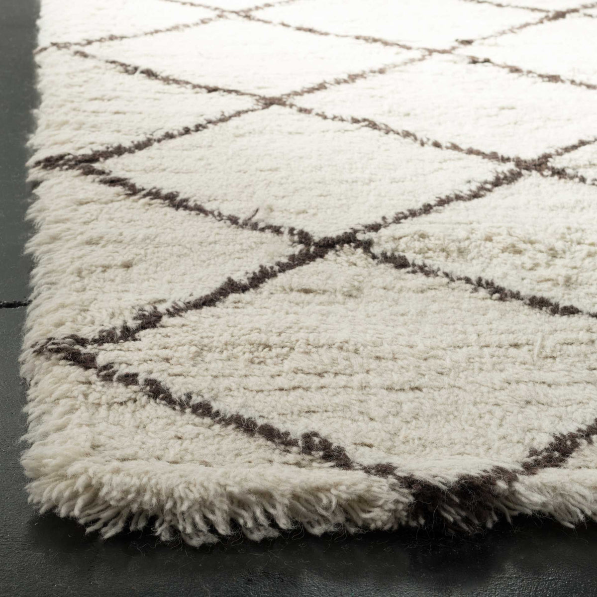 Thick ivory wool fibers and dark brown lattice lines meet at a shaggy rug corner