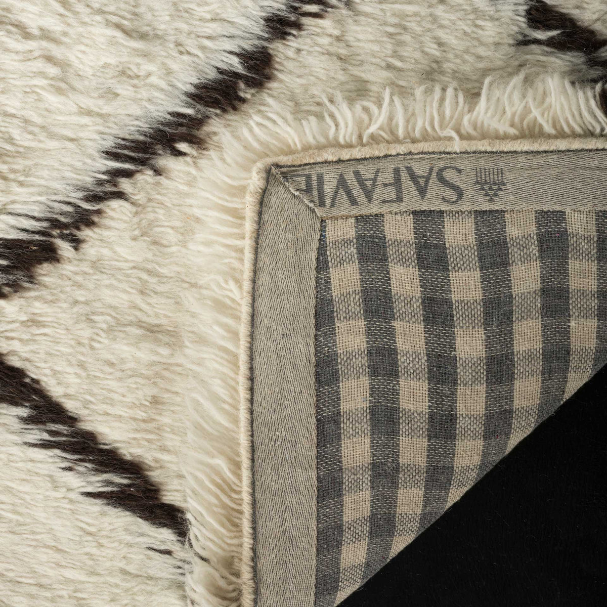 A folded corner reveals checked woven backing beneath plush ivory wool and dark brown lines