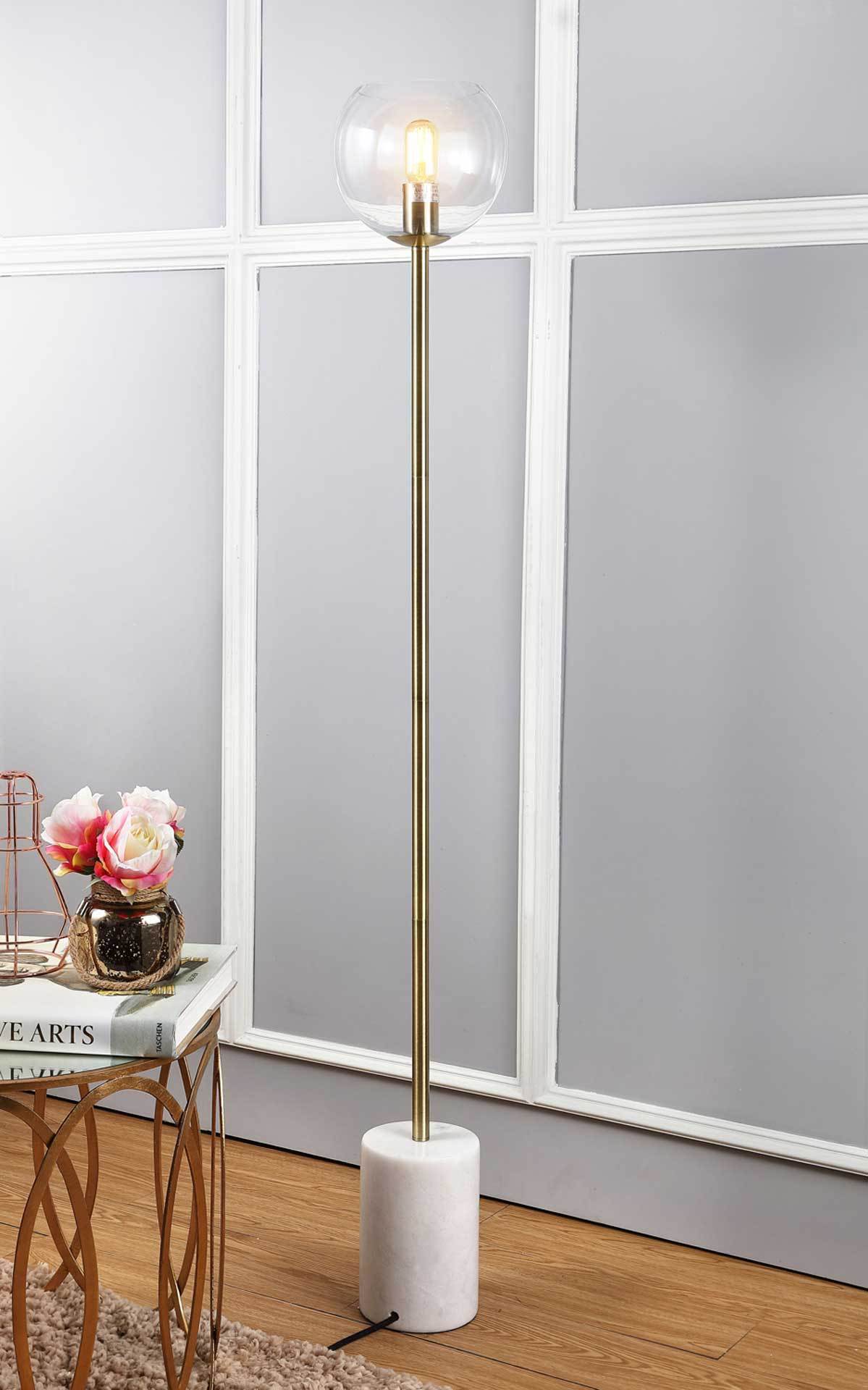 Warm light shines through a clear globe atop a gold stem and sturdy marble base