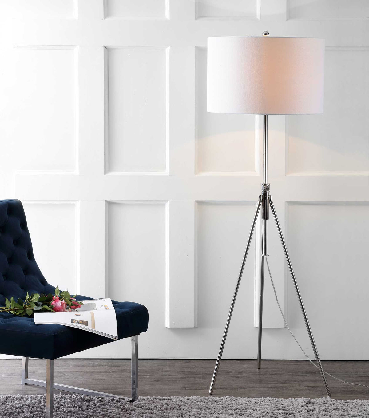 A glowing white shade casts warm light over a silver tripod lamp beside a navy chair