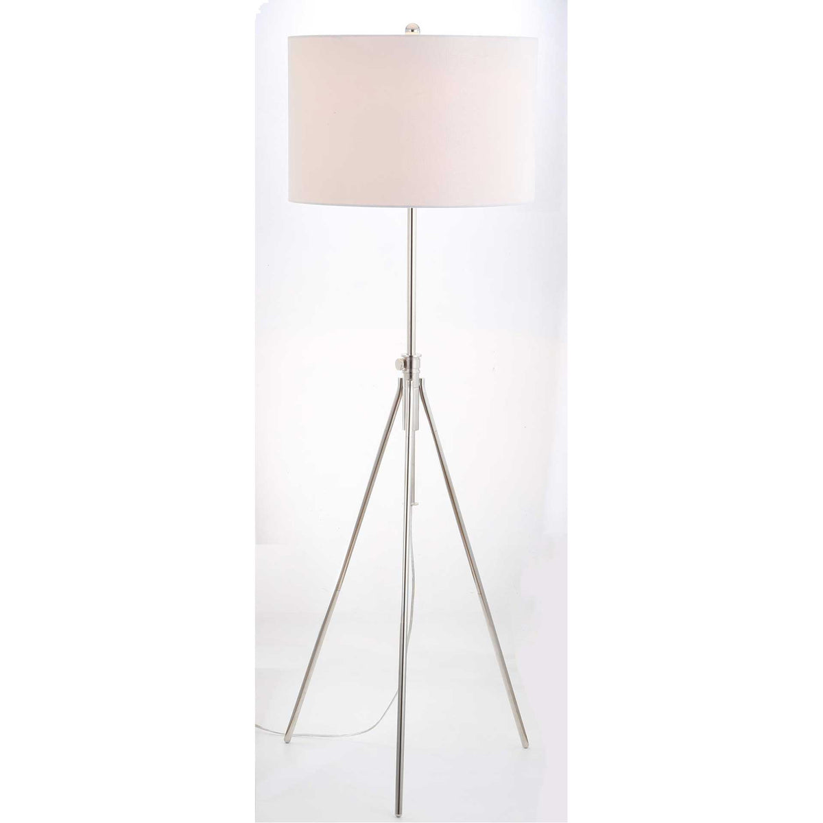 Warm light glows through the white drum shade above a slender silver tripod base