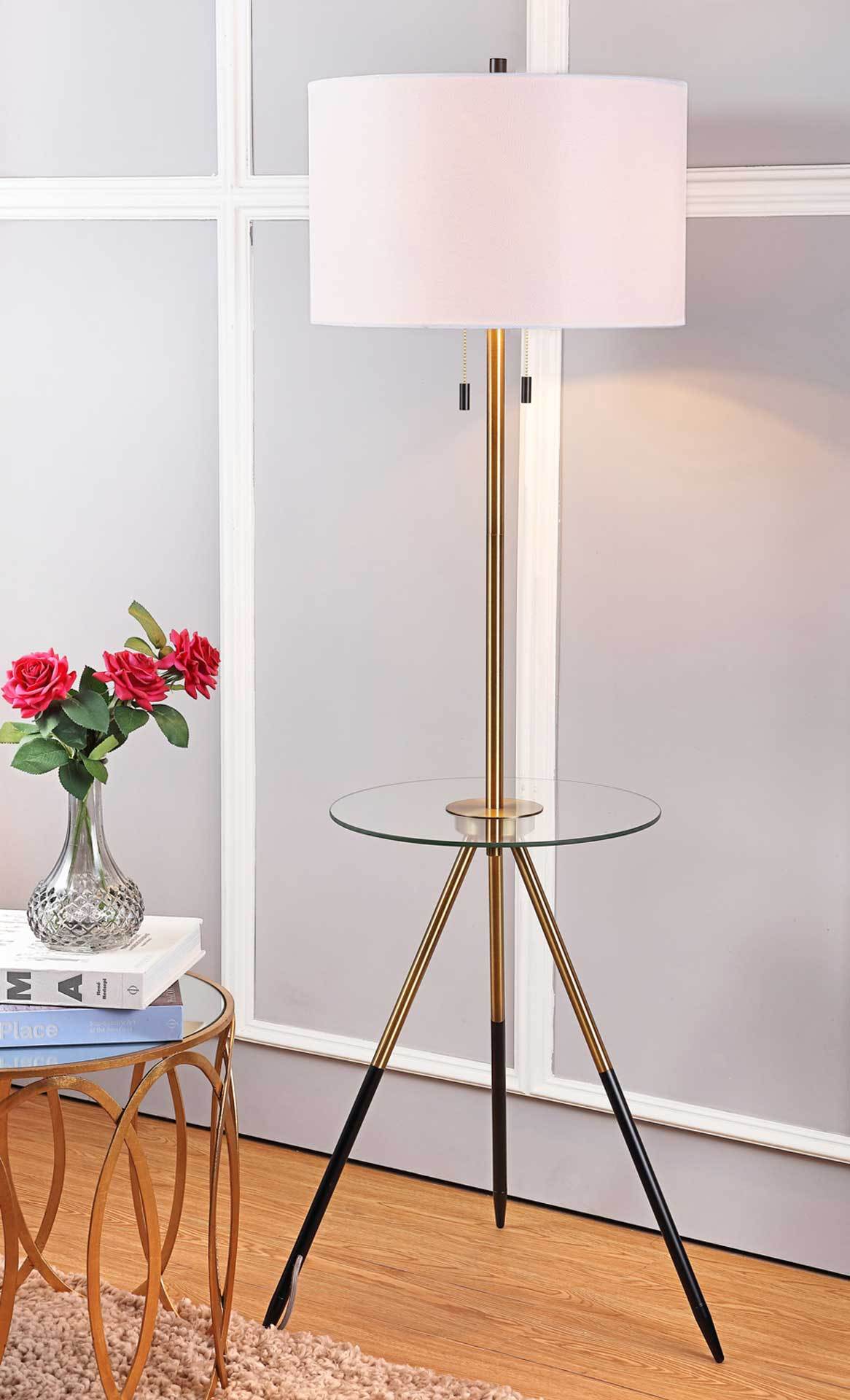 Warm light glows through the drum shade above a round glass tabletop and slender tripod base