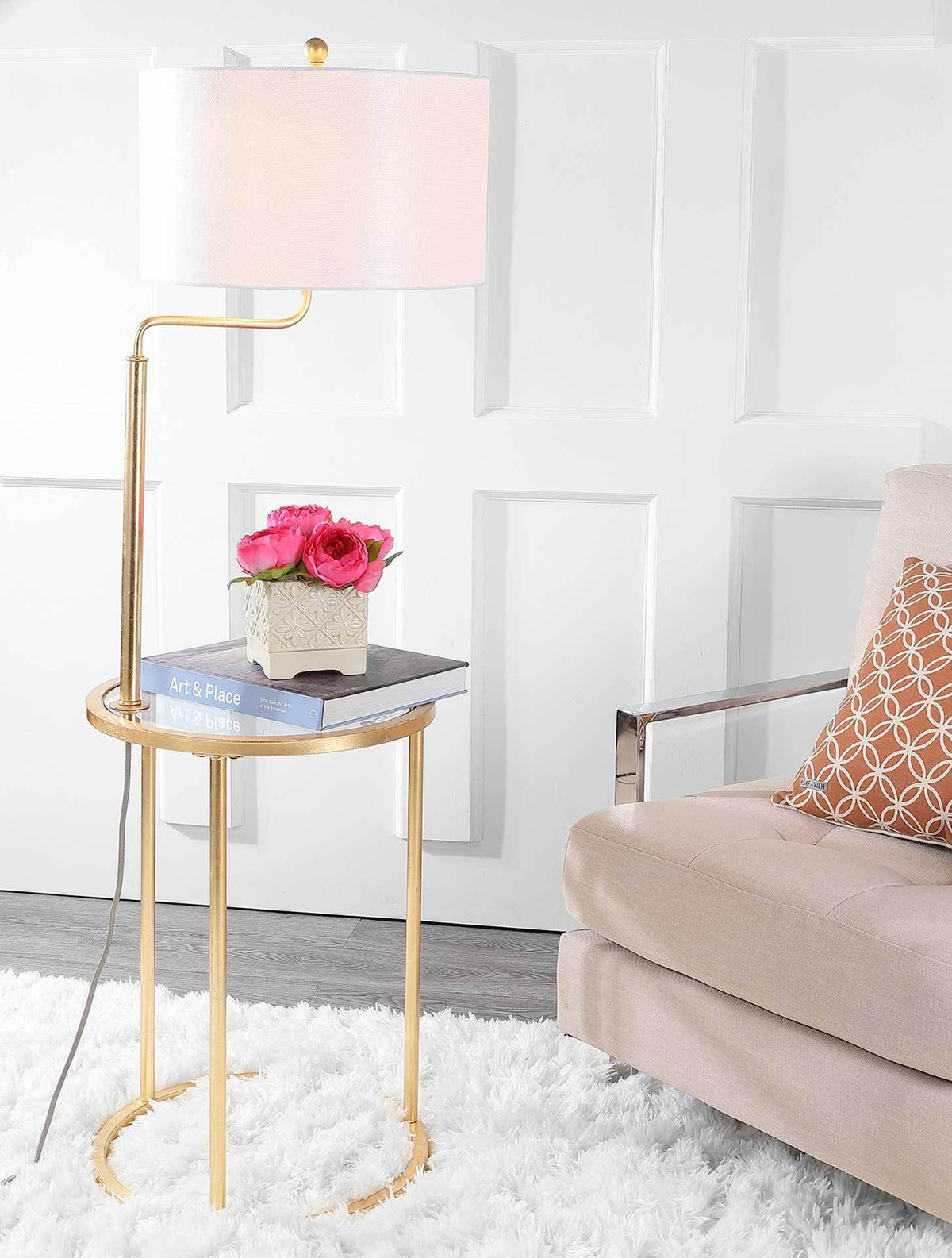 A glowing off-white shade brightens a gold-framed side table with books and flowers beside a sofa.