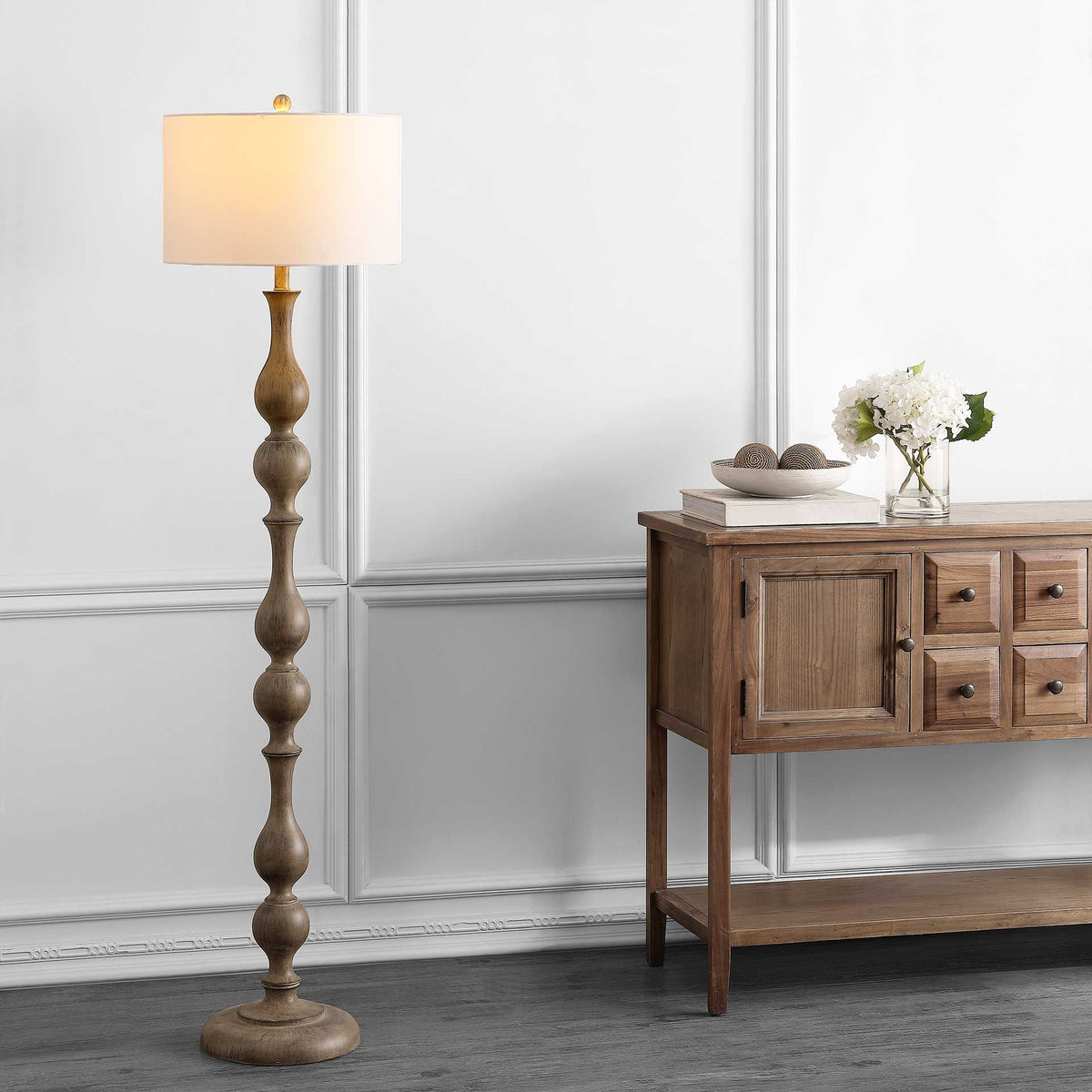 Soft light fills the drum shade atop a tall floor lamp with a sculpted brown column