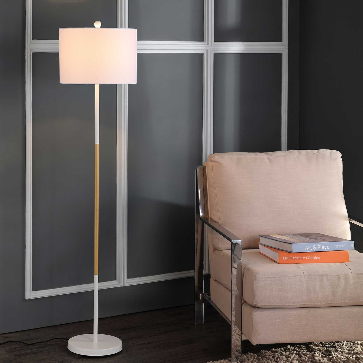 A softly glowing drum shade brings warm light beside an armchair, supported by a slender two-tone stem.