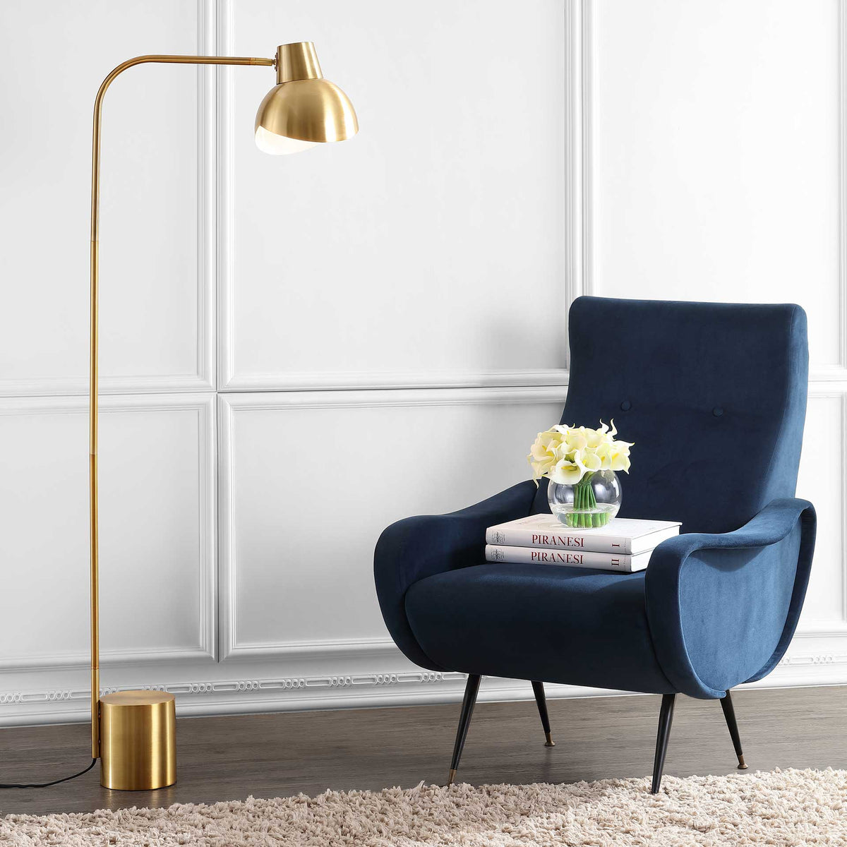 Gold floor lamp casts a soft glow beside a deep blue chair in a cozy reading nook