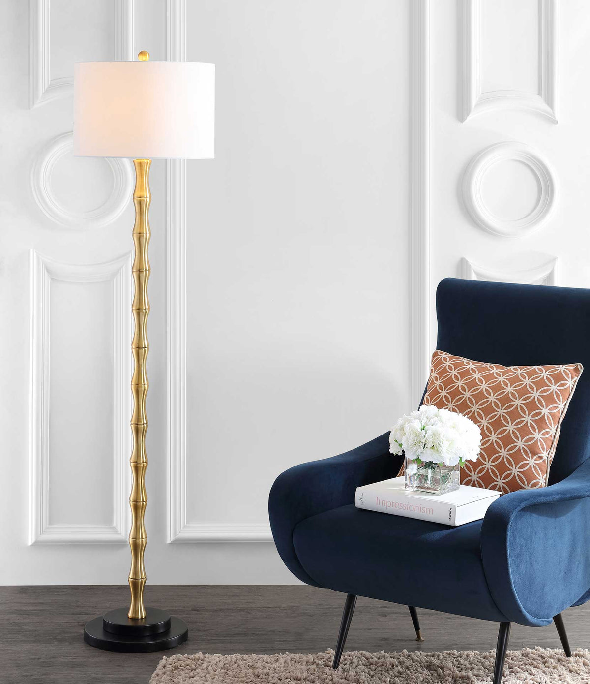Warm light shines through the off-white drum shade above a slender sculpted gold stem