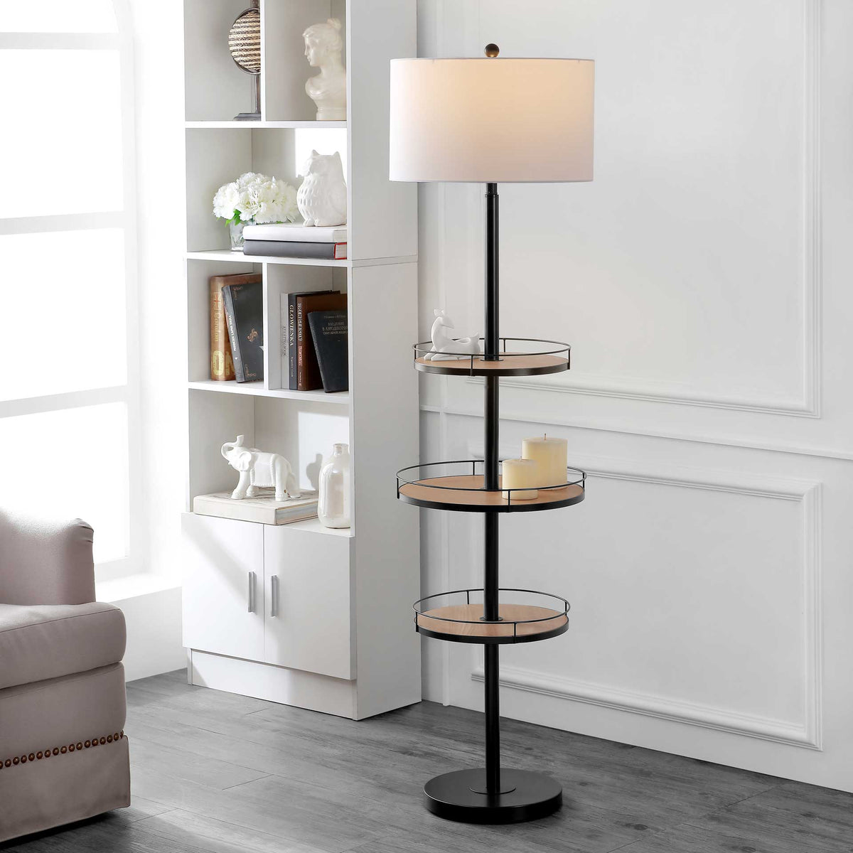 A softly glowing drum shade tops a black floor lamp with three wood-tone display shelves
