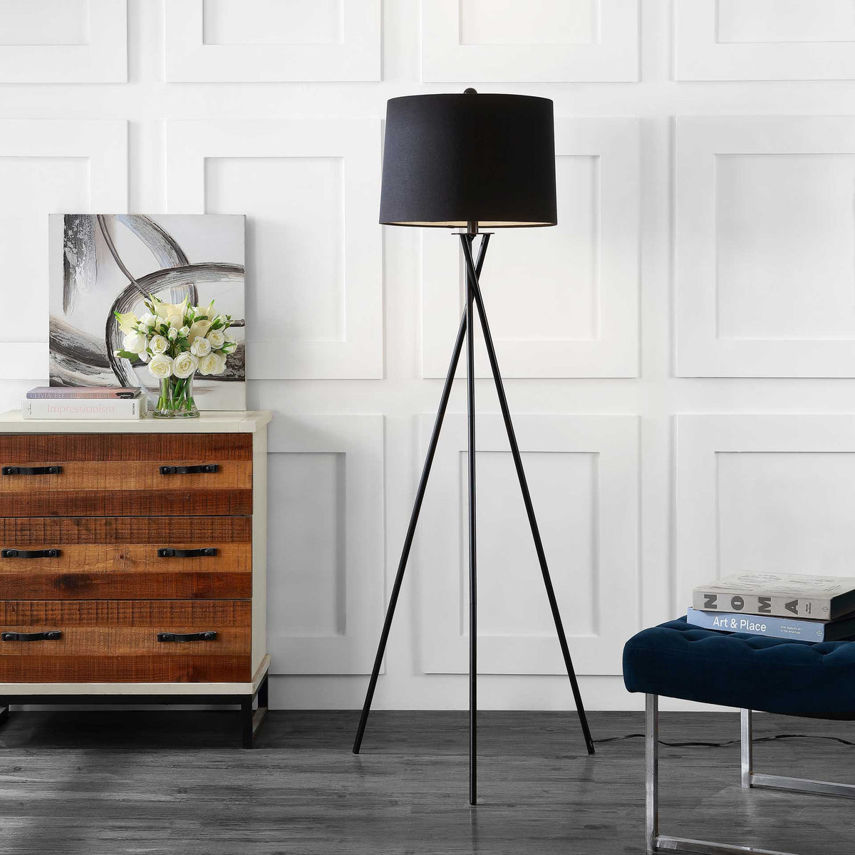 Warm light peeks beneath the black shade of a slender iron tripod floor lamp