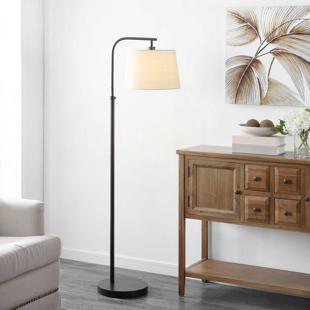 Warm light shines through the tapered shade of a slender floor lamp with a curved bronze-finished arm