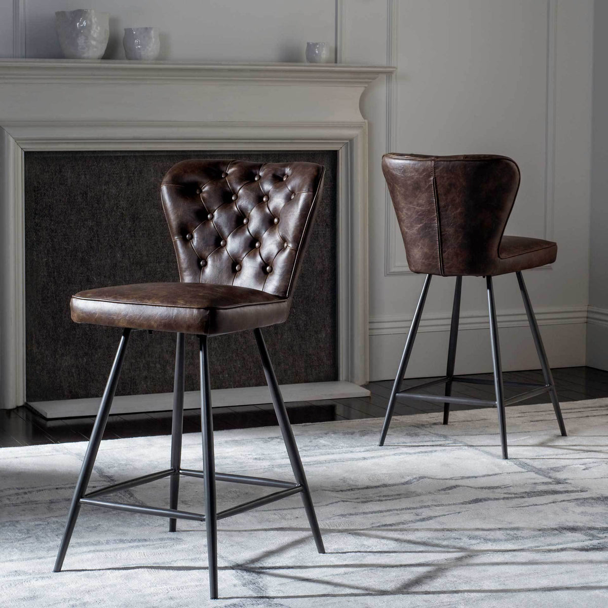 Two brown counter stools add warmth with tufted upholstery and sleek metal legs beside a fireplace.