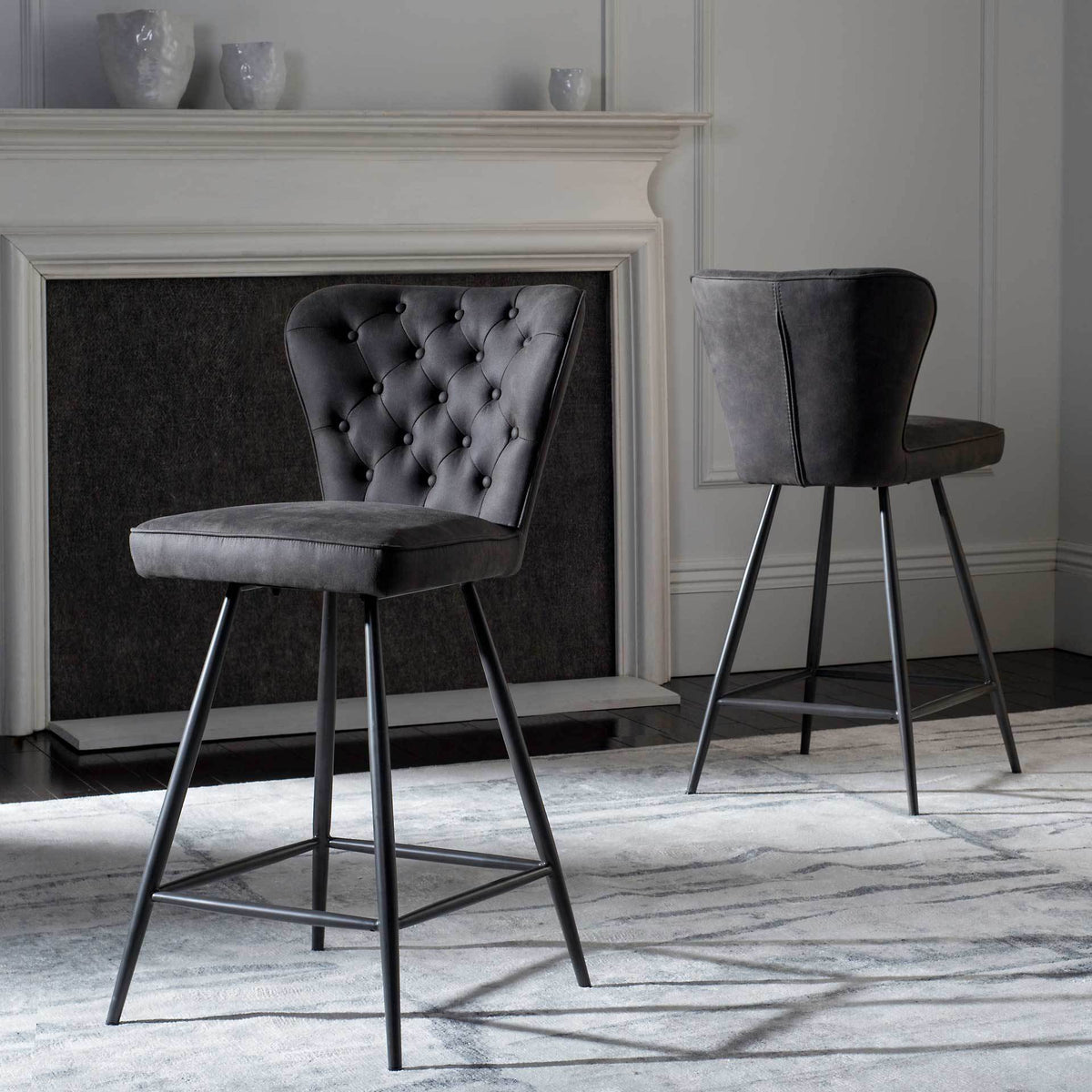 Two gray counter stools bring tufted texture and streamlined metal legs to a fireplace setting.